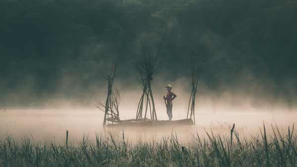 Lone fisherman on a traditional boat amidst the morning fog at Lake Tamblingan, Bedugul, Bali.