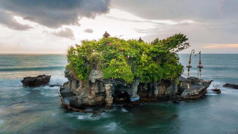 Verdant islet Tanah Lot Temple in Bali with waves crashing at dusk