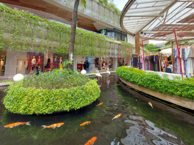 Elegant shopping boutiques along a serene koi pond in Kuta, Bali, with lush greenery and open-air ambiance.