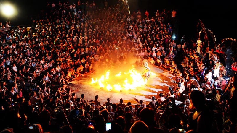 A vibrant Uluwatu Kecak Dance performance at sunset with a large audience in Bali