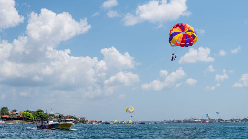 Visitors enjoy parasailing over the blue Bali sea with clear skies.