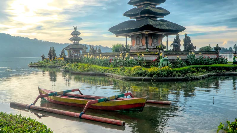 Serene morning at Ulun Danu Beratan Temple with traditional boat on calm lake waters.