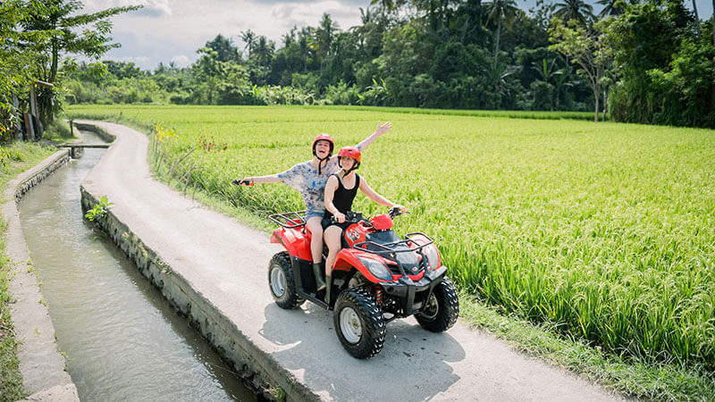 Two people on an ATV enjoying a ride through Bali's lush green rice fields.