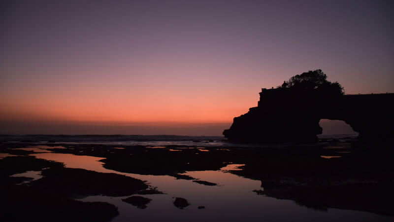 Stunning sunset over Tanah Lot Temple, Bali with red sky and silhouette of the temple in the foreground.