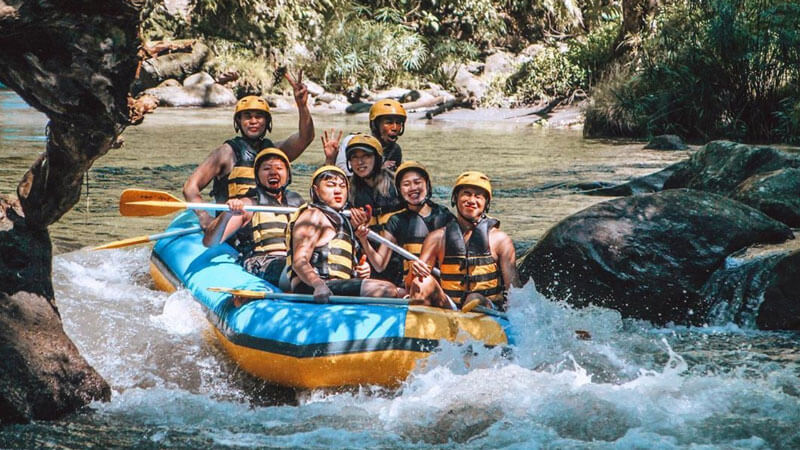 Group of adventurers river rafting on the Ayung River in Bali with helmets and paddles