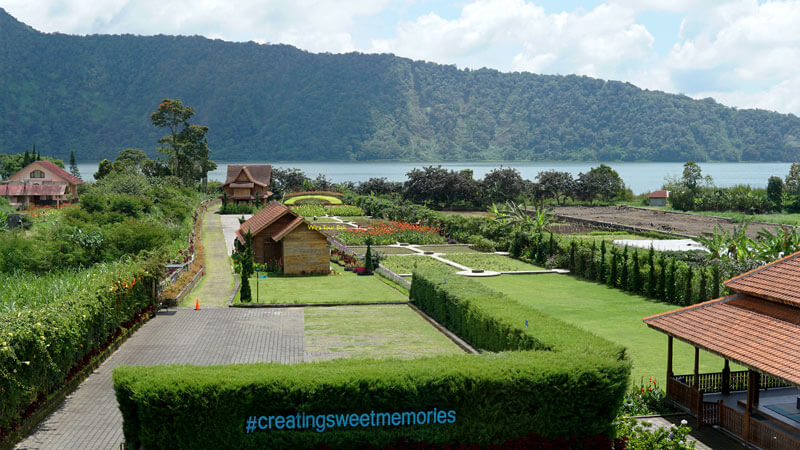 Scenic view of Bedugul's lush green landscape with Lake Bratan in the background, framed by a hashtag #creatingsweetmemories.