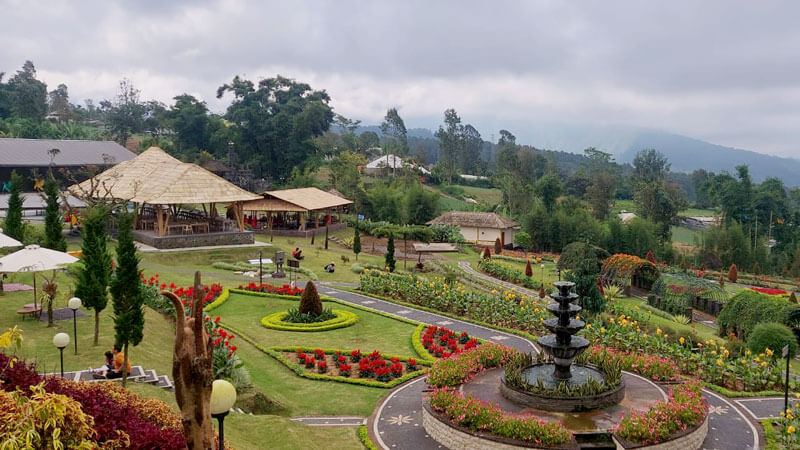 Panoramic view of The Blooms Garden with vibrant flowers, a central fountain, and traditional thatched huts in Bedugul, Bali.