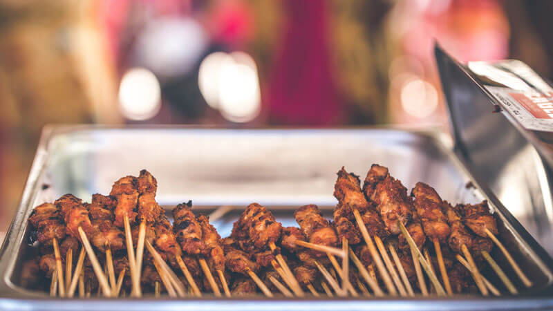 Grilled meat skewers on display at a Balinese street food stall with blurred background.