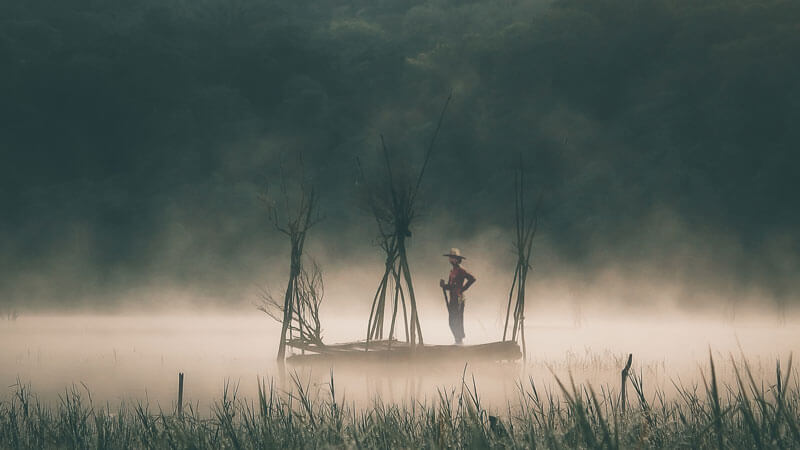 Silhouette of a solitary fisherman on misty Lake Tamblingan at dawn, Bali.