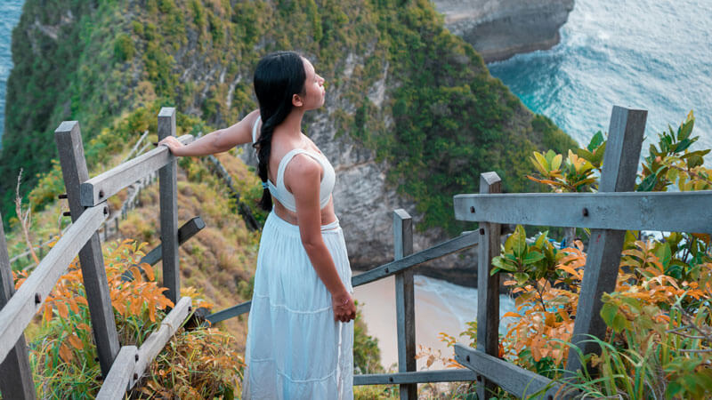 Woman overlooking a scenic Bali coastline from a wooden viewpoint