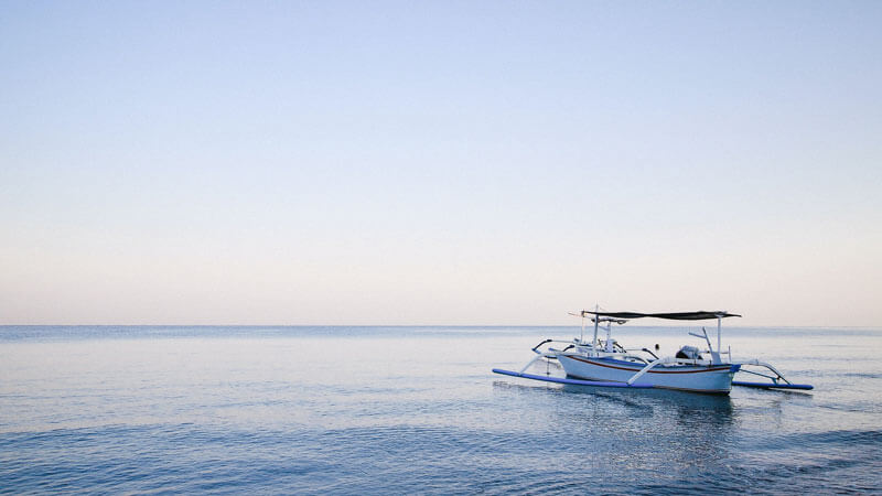 Traditional Balinese boat floating on the calm waters of Lovina Beach at dawn