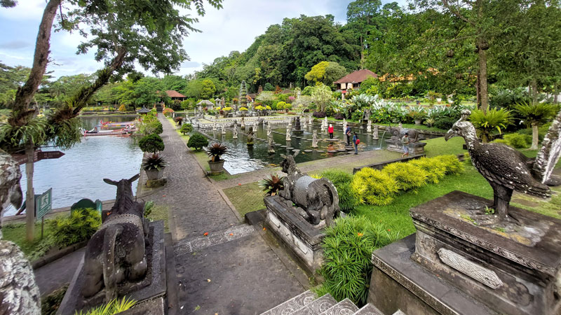 Panoramic view of Water Palace with its stone sculptures, tiered water ponds, and visitors enjoying the tranquil setting in Karangasem, Bali.