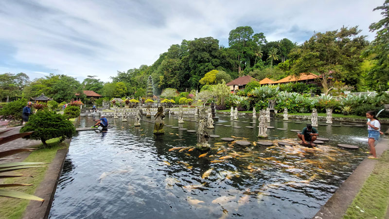 Visitors enjoying the vibrant koi pond and ornate water features at Water Palace, a serene sanctuary reflecting Balinese cultural heritage in Karangasem.