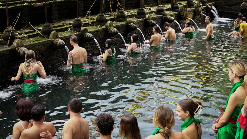 Tourists performing the sacred purification ritual in a Balinese holy spring temple, using water from ancient stone fountains.