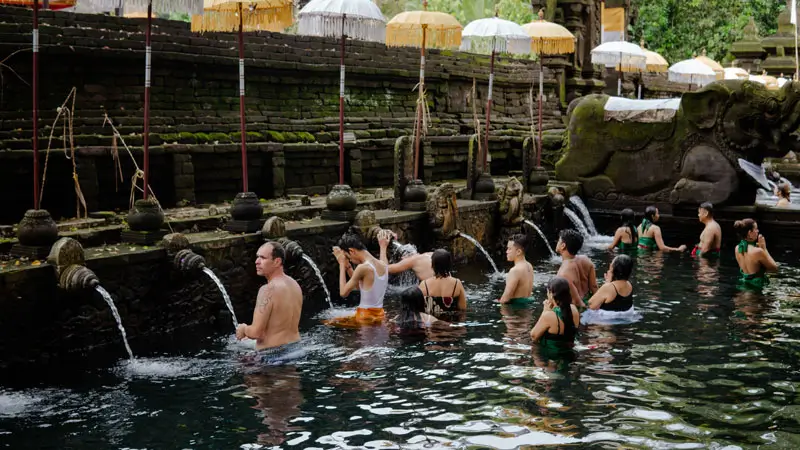 Travelers participating in the sacred Melukat purification ritual at a famous Balinese water temple, known for its spiritual cleansing pools.