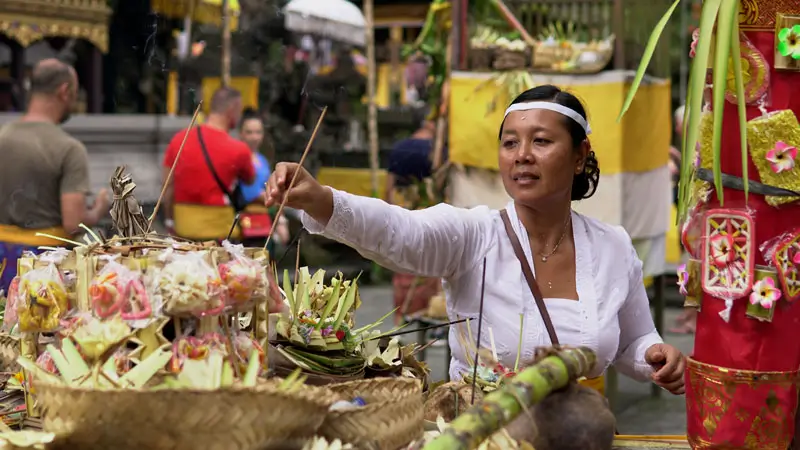 A Balinese woman making an offering (Canang Sari) at Tirta Empul Temple during a cultural ceremony in Bali.