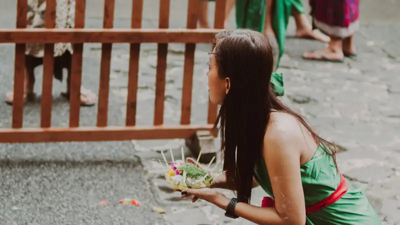 A woman preparing a Canang Sari offering before participating in the Melukat purification ritual at a sacred Balinese water temple.