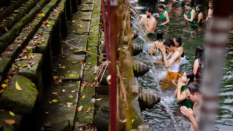 Visitors performing the sacred Melukat purification ritual at a holy Balinese water temple, washing away negative energy in the spiritual cleansing pools.