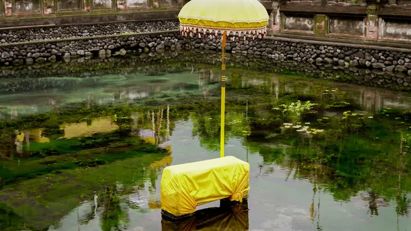 Sacred spring water at Tirta Empul Temple in Bali, believed to have healing properties, with a traditional Balinese umbrella adorning the water source.