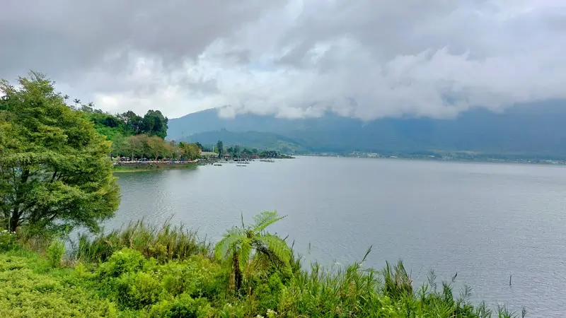 Quiet shoreline of Lake Beratan Bedugul Bali under cloudy skies with calm water and highland mist