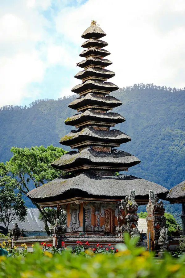 Tall 11-tiered Meru tower at Ulun Danu Beratan Temple in Bedugul, framed by mountain scenery and temple statues