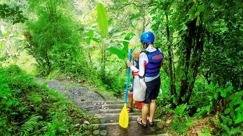 Traveler in rafting outfit descending mossy stairs to Ayung River in Ubud.