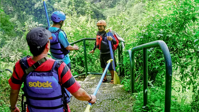 Group of Ayung rafters descending jungle stairs with paddles and safety gear in Ubud