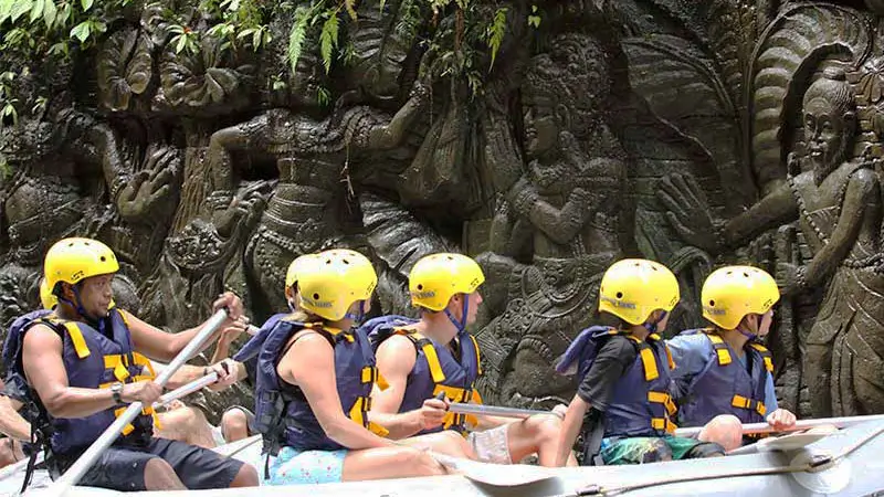 Group rafting near intricate Balinese cliff carvings along Ayung River in Ubud Bali.