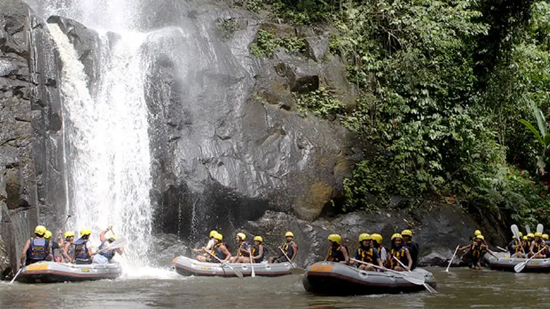 Travelers rafting near a jungle waterfall on the Ayung River surrounded by tropical greenery.