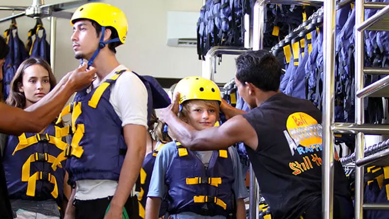 Rafting guide fitting helmet and vest on a child before Ayung River rafting in Ubud.
