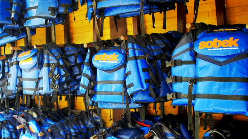 Organized rack of blue life jackets at rafting operator basecamp