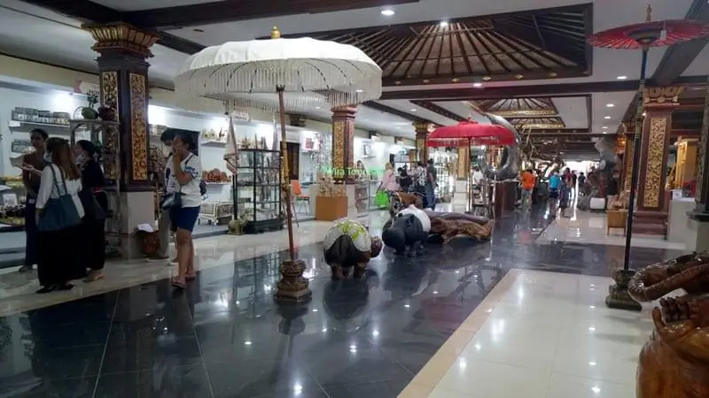 Visitors browsing handicraft stalls and sculptures inside an indoor gallery