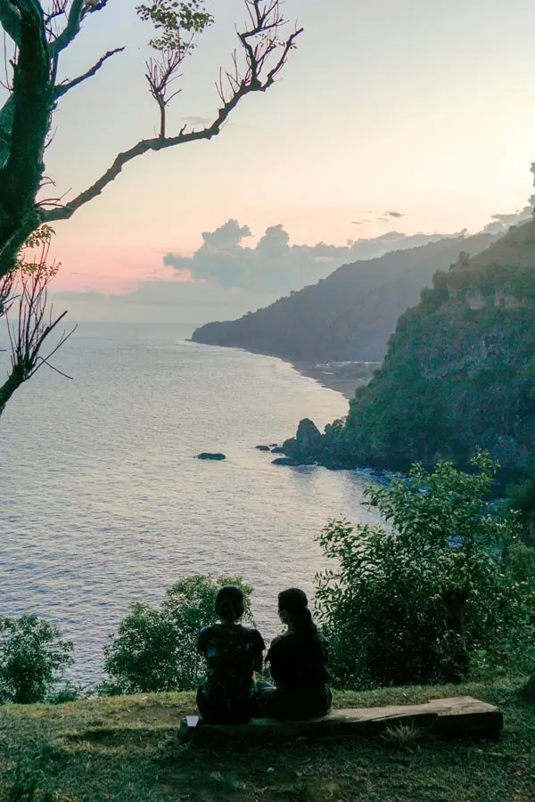 Couple sitting on a bench overlooking a steep coastal cliff at dusk