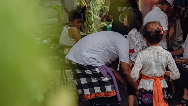Children in Balinese temple outfits with lace tops, sarongs, and colourful sashes beside an adult
