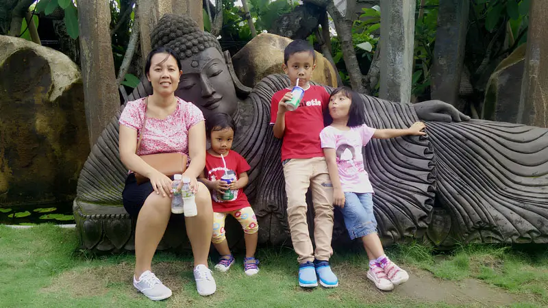 Mother and three children relaxing by reclining Buddha statue at Big Garden Corner Denpasar.