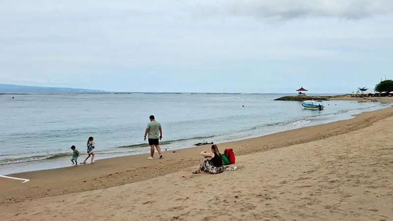 Family with children playing on calm Sanur Beach shoreline in Bali