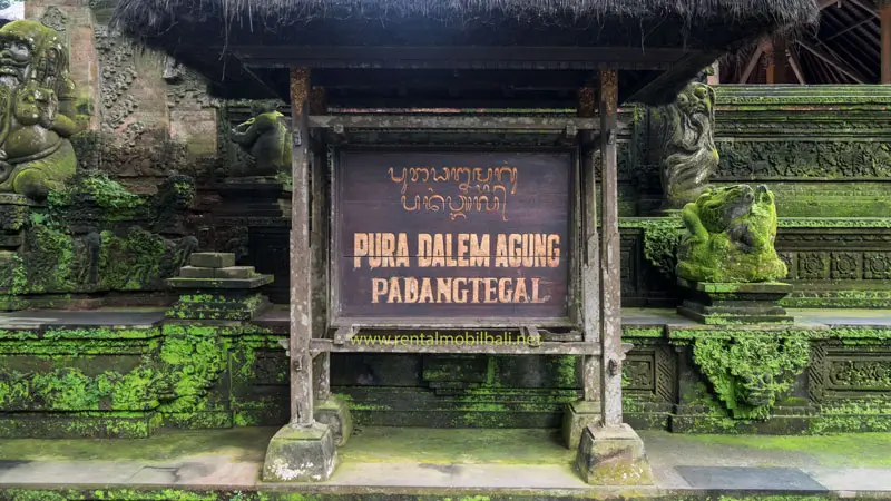 Wooden sign of Pura Dalem Agung Padangtegal with mossy walls and stone carvings in Ubud