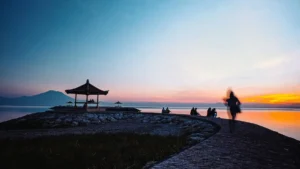 Sunrise at Sanur Beach near Denpasar with families sitting by a seaside pavilion and calm water