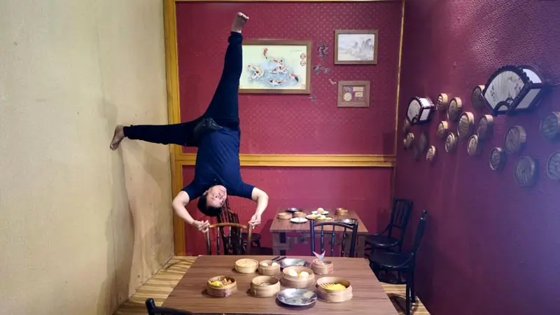 Visitor posing upside down in dining room set at Upside Down World Bali Denpasar