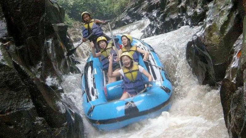 Four people in a blue raft passing through narrow rocky rapids.