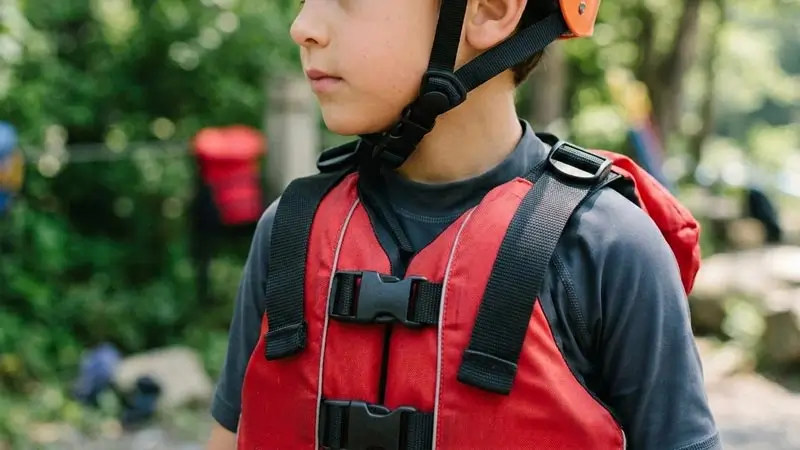 Child wearing a fitted helmet and life jacket before kids rafting