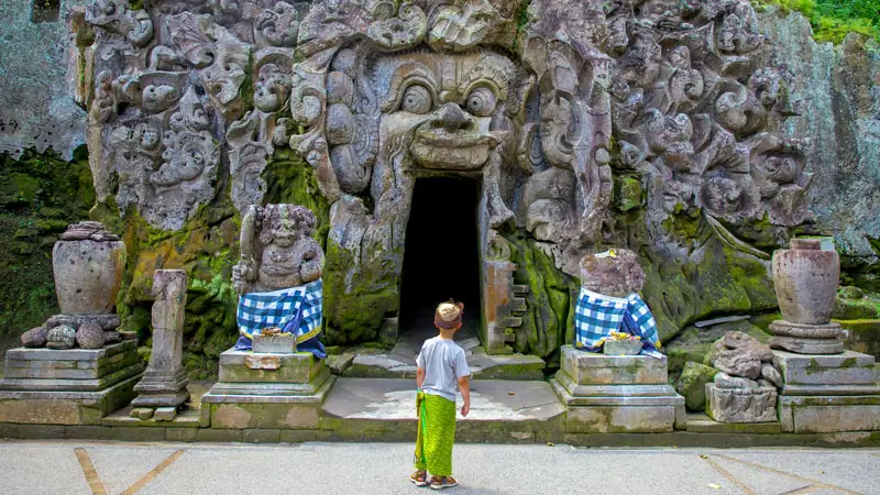 Child in a sarong facing the carved Goa Gajah temple entrance